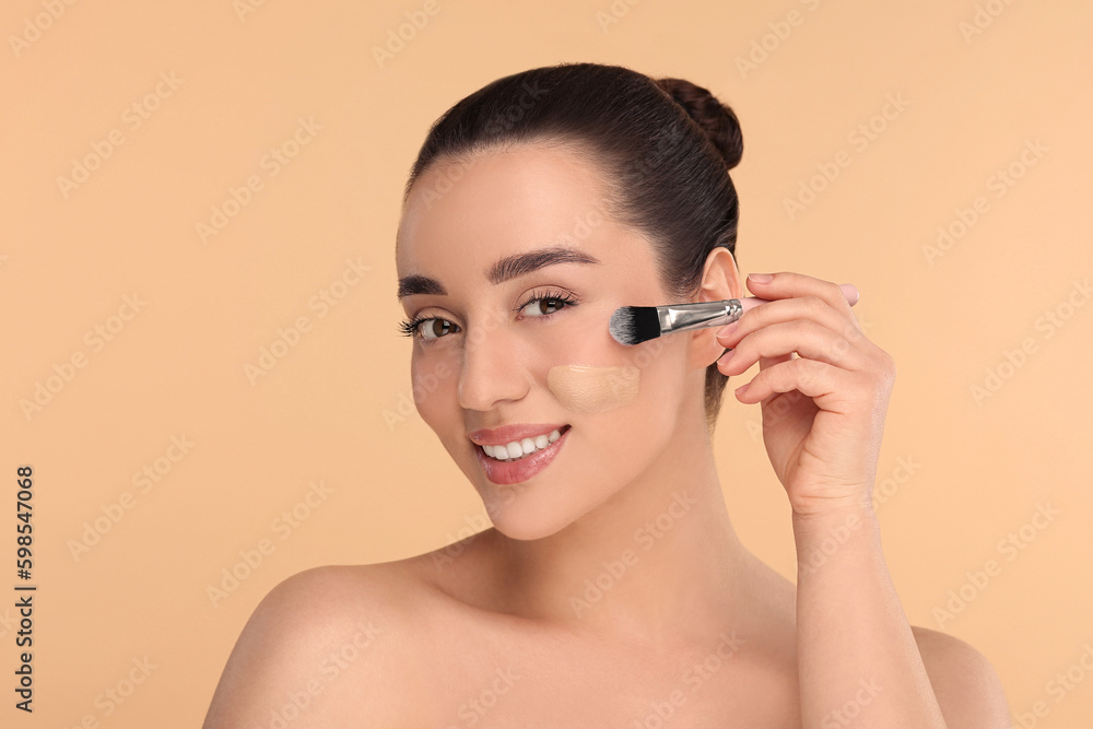 Woman applying foundation on face with brush against beige background Woman applying foundation on face with brush against beige background