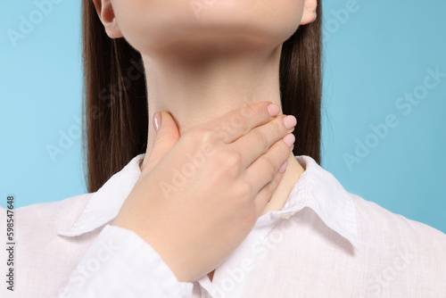 Woman with sore throat on light blue background  closeup