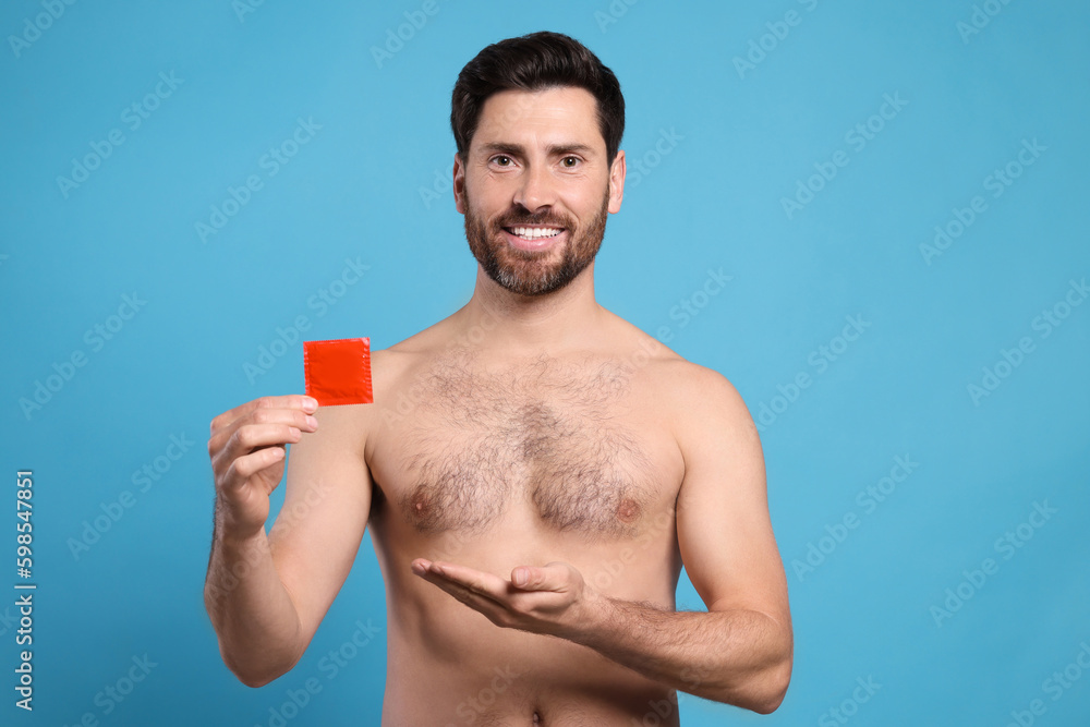Naked man holding condom on light blue background. Safe sex Naked man holding condom on light blue background. Safe sex