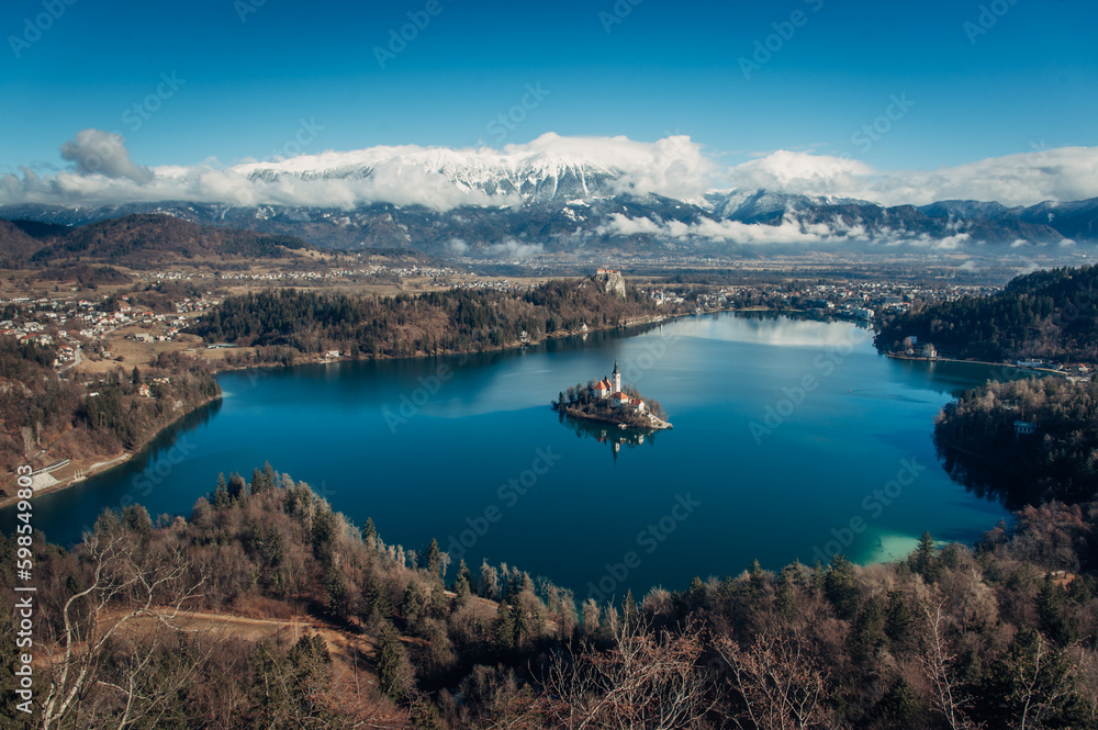 A stunning aerial view of Lake Bled, Slovenia with the Julian Alps in the background, and a few clouds hovering above.