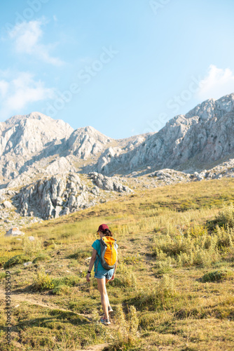 a traveler with a backpack walks along a mountain path. a girl walks in the mountains.