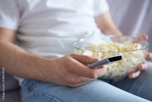 Man watching TV and eating popcorn at home on the couch  front view.
