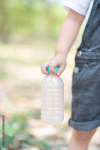 Little boy Hand holding recyclable plastic bottle in garbage bin with sunset light