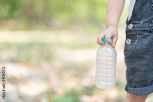 Little boy Hand holding recyclable plastic bottle in garbage bin with sunset light