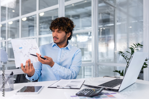 Upset financier showing online report, man working inside office nervously showing document, hispanic man in online meeting using laptop for remote communication and video call.