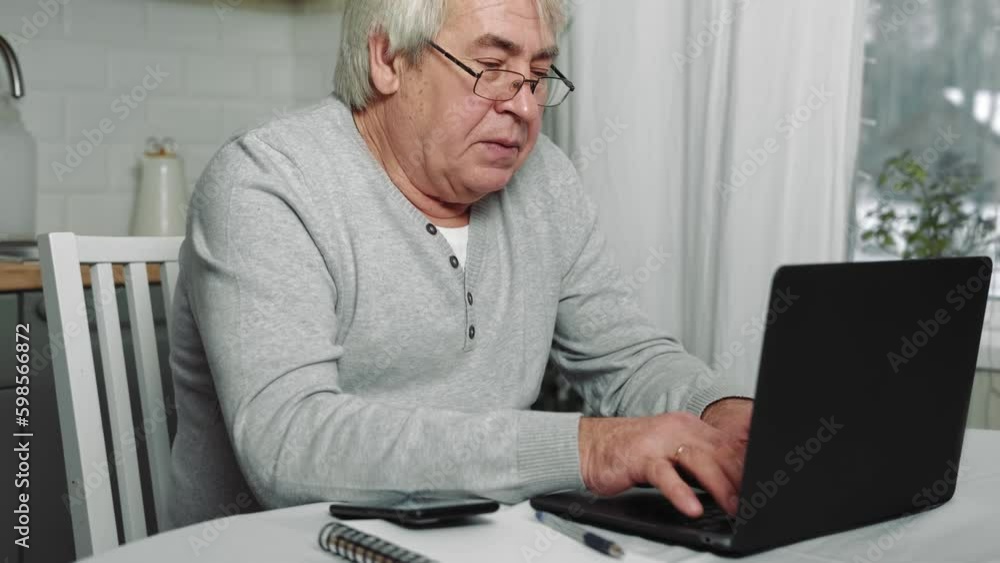 Senior male business owner in glasses sitting at desk in front of laptop. Successful older male working at home. Grey haired 60s - 70s Aged busy man typing keyboard, drinking coffee. Distance office Senior male business owner in glasses sitting at desk in front of laptop. Successful older male working at home. Grey haired 60s - 70s Aged busy man typing keyboard, drinking coffee. Distance office