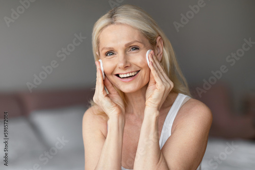 Fotografia Lovely mature lady using cotton pads to remove makeup, aged woman applying natur