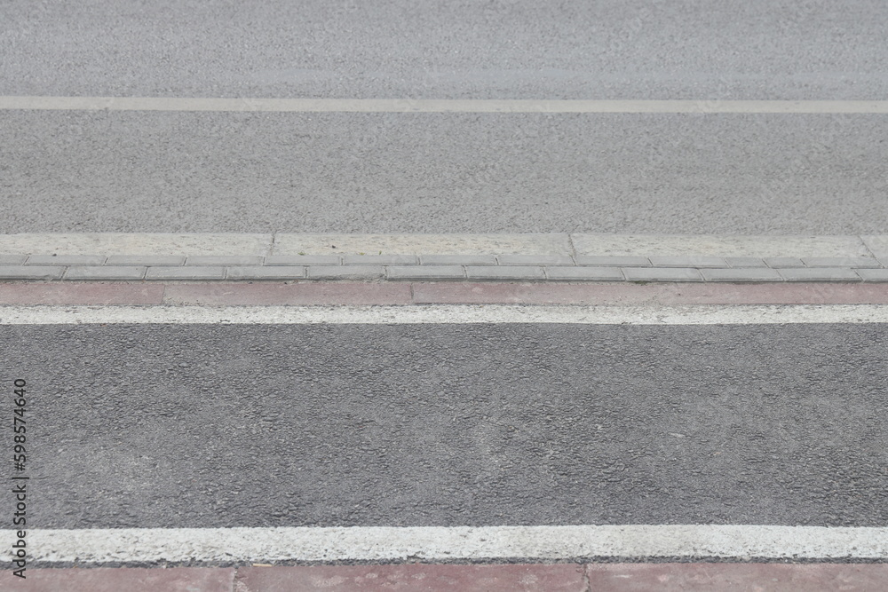 Fototapeta premium A street border painted in white and black on the background of the road and green foliage in the summer closeup. Road safety, minimalism.