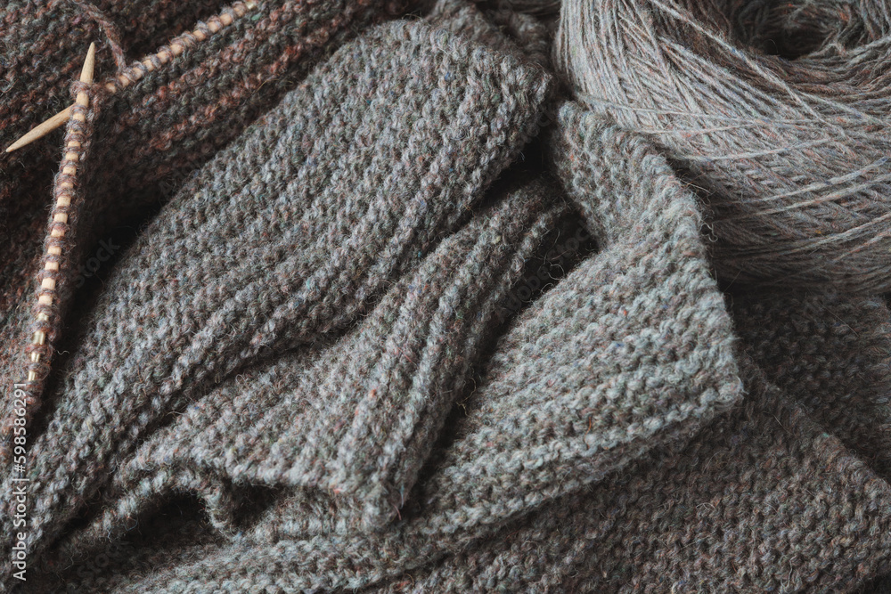 Unfinished gray scarf, knitting needles and a round skein of wool. Unfinished gray scarf, knitting needles and a round skein of wool.