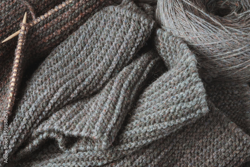Unfinished gray scarf, knitting needles and a round skein of wool.