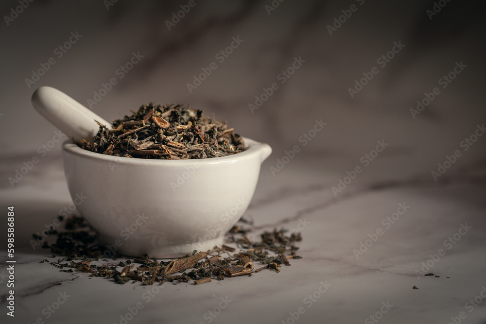 Closeup of Dry Bhringraj (Eclipta prostrata) leaves, in white ceramic mortar and pestle. Front view on marble background. Closeup of Dry Bhringraj (Eclipta prostrata) leaves, in white ceramic mortar and pestle. Front view on marble background.