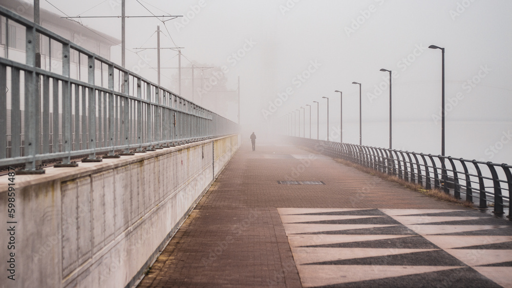 A silhouetted person walks down a misty path in an urban setting