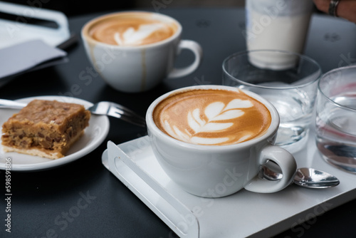 Two cups of specialty coffee flat white or cappuccino with a flower on top, bake table in a hipster cafe  