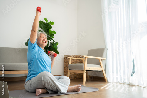 Asian senior woman lifting dumbbell for exercise and workout at home. Active mature woman doing stretching exercise in living room. Exercise Active and healthy for older, elder, and senior concept.