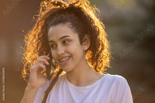 Cute girl talking on mobile phone in park at sunset