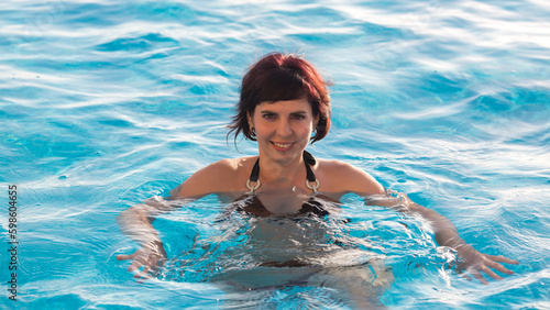 Young woman bathes in the blue water of the pool, close-up.