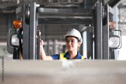 Professional female industrial driver operating forklift truck in logistic warehouse. Asian woman wear safety helmet working at cargo storage distribution driving forklift transport goods for delivery photo