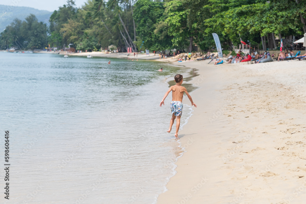 Rear view of a little boy having fun running on a tropical sandy beach Rear view of a little boy having fun running on a tropical sandy beach