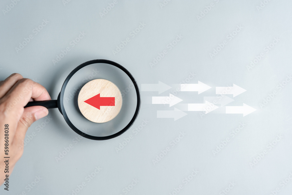 Hand holding magnifier focus to Red arrow and different direction facing opposite direction with