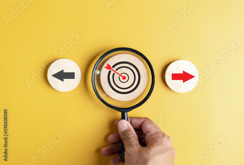 Hand holding magnifier focus to dardboard with Red arrow and different direction facing opposite direction with black arrow for business disruption and technology transformation. photo