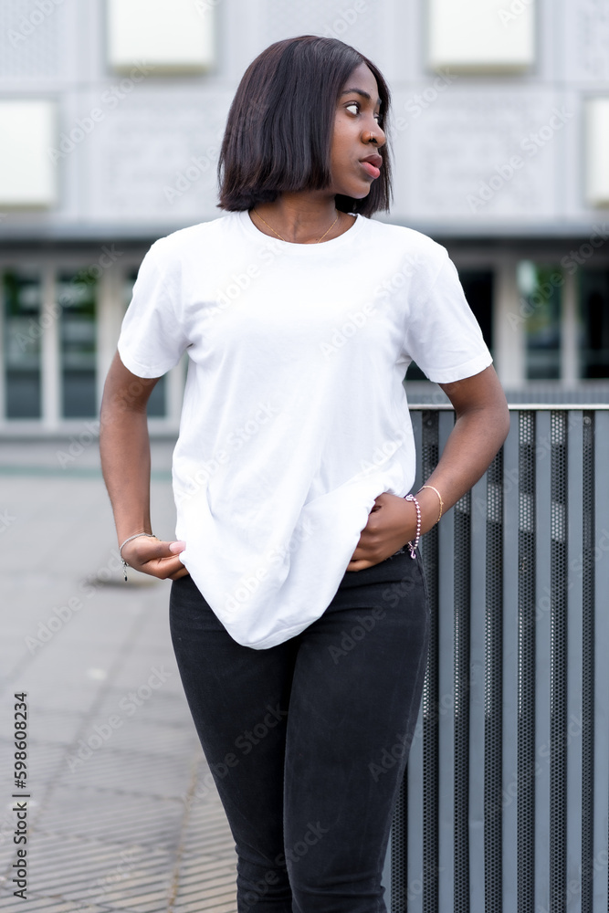 City vibes and casual fashion: A young black woman poses in a white t-shirt and black pants against a sleek urban backdrop