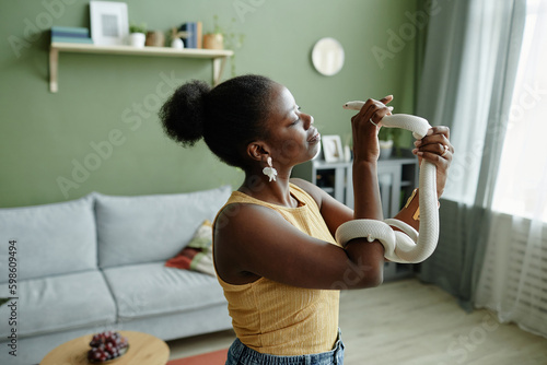 White rat snake enlacing arm of young African American female owner holding pet while enjoying animal assisted therapy in living room photo