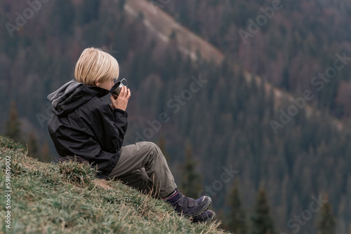 Portrait of tourist boy in mountains resting on hillside with cup of tea. Hiking with child in the fall. Active recreation. © somemeans