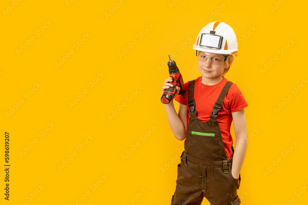 Portrait of little boy pretends to drill wall with drill, yellow isolated background. Boy teenager as builder worker. Copy space, mockup