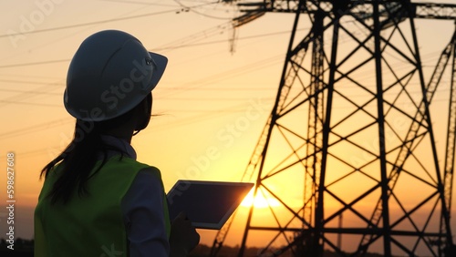 silhouette electrician engineer hand holding tablet. electric power industry high voltage. employee electrician works sunset. energy concept. electric tower high voltage. power line. work tablet sun