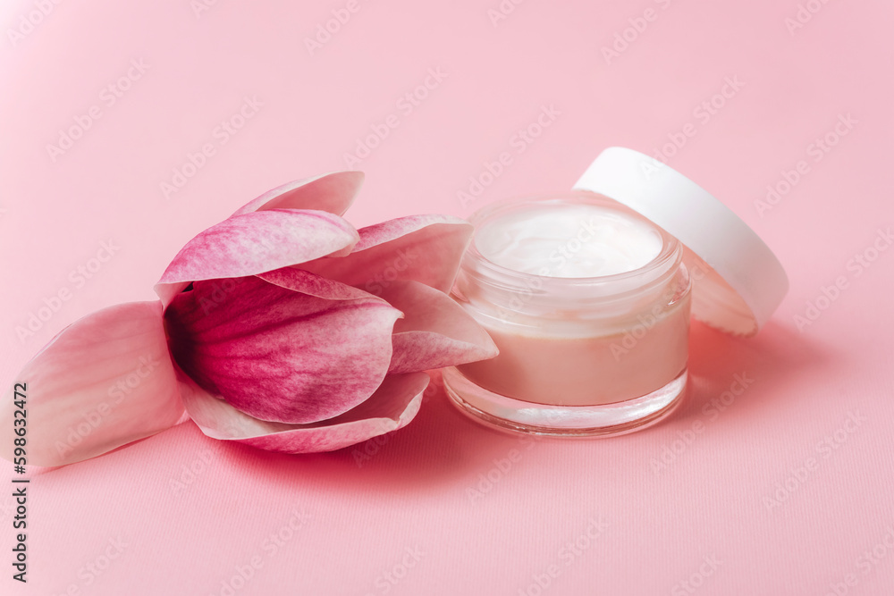 Cosmetic cream jar and magnolia flower on pink background. Skin care, beauty treatment concept. Closeup Cosmetic cream jar and magnolia flower on pink background. Skin care, beauty treatment concept. Closeup