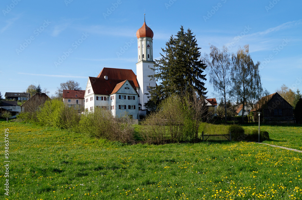 ancient catholic German church Saint Nikolaus in the Bavarian village Rechbergreuthen in Winterbach, Guenzburg, Bavaria, Germany on dandelion meadow on a sunny spring day with blue sky