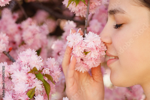 Close Up View of the Young Beautiful Caucasian Girl Standing in the Blooming Sakura Park, Posing and Inhaling the Tree Aroma. Femininity and Natural Beauty Concept