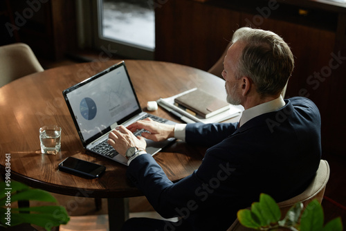 Fototapeta Naklejka Na Ścianę i Meble -  High angle view of businessman working over report online using his laptop while sitting at table in coffee shop