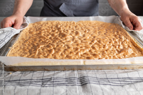 Fresh baked sponge cake for making swiss roll on a baking sheet is held by a womans hand