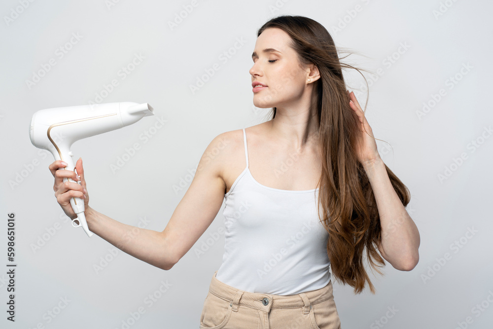Young beautiful confident woman using hair dryer isolated on white background Young beautiful confident woman using hair dryer isolated on white background
