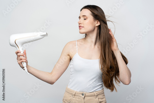 Young beautiful confident woman using hair dryer isolated on white background 