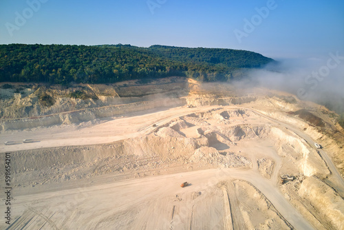 Aerial view of open pit mining of limestone materials for construction industry with excavators and dump trucks