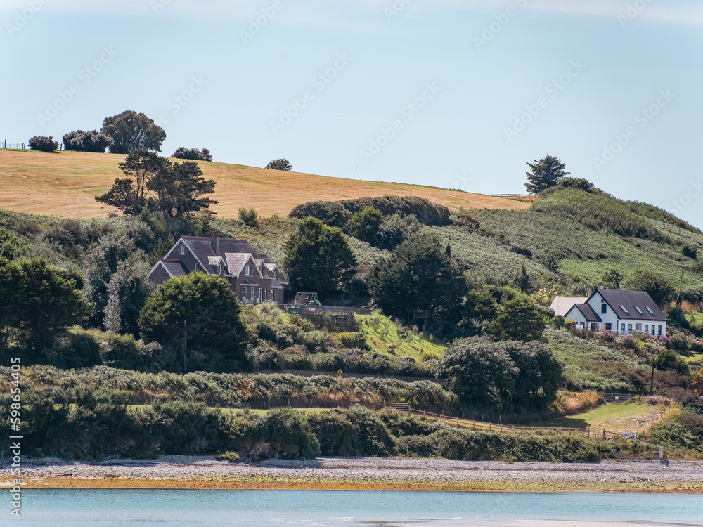 Houses on the shore of the gulf of Ireland on a sunny summer day. Hilly Irish landscape, nature, house near green trees and water.