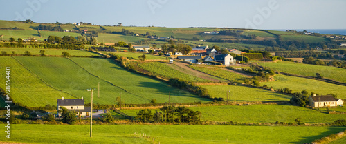 farm fields in the south of Ireland on a summer evening. Agricultural Irish landscape. Pastures for livestock, house on green grass field.