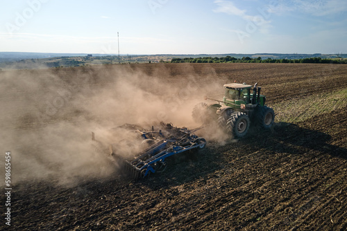 Aerial view of tractor plowing agriculural farm field preparing soil for seeding in summer