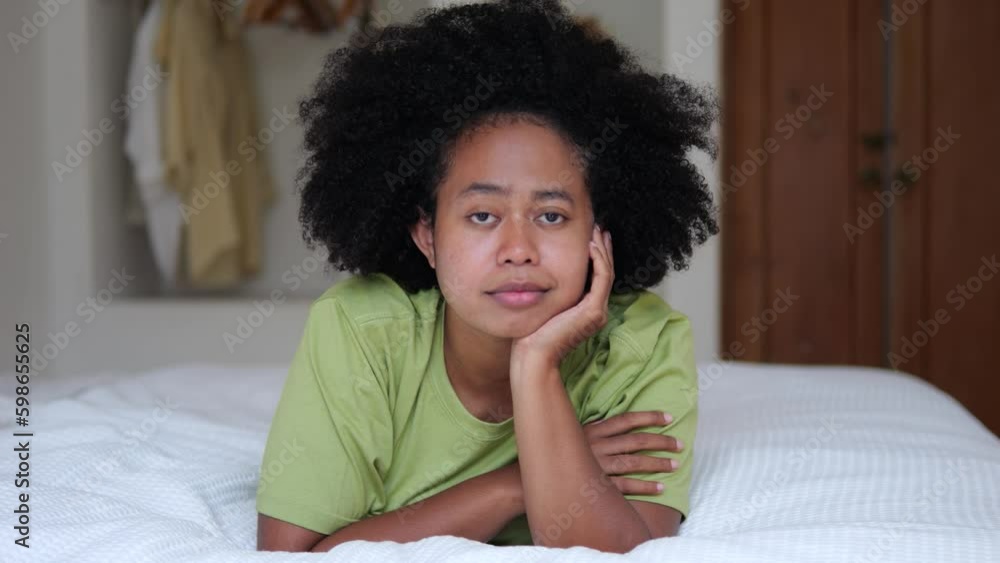 Curly attractive black African-American teen girl lies on bed on her stomach and looks at camera. Calm, quiet, serene black multinational teenage girl lies with her face propped on her Generative AI Curly attractive black African-American teen girl lies on bed on her stomach and looks at camera. Calm, quiet, serene black multinational teenage girl lies with her face propped on her Generative AI