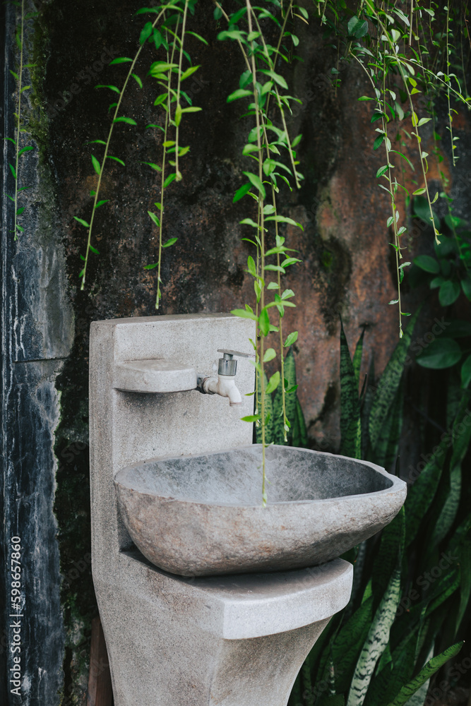 Concrete washstand against the background of a textured wall and green vines. Stylish fannaya with plants. Washing hands outside