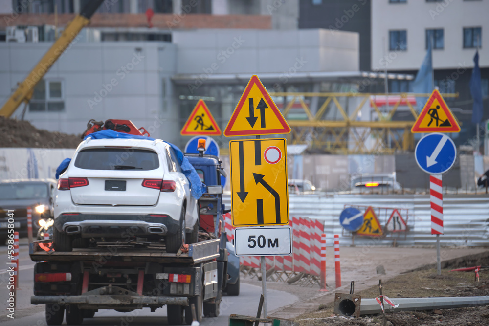 Roadworks warning traffic signs of construction work on city street and slowly moving cars