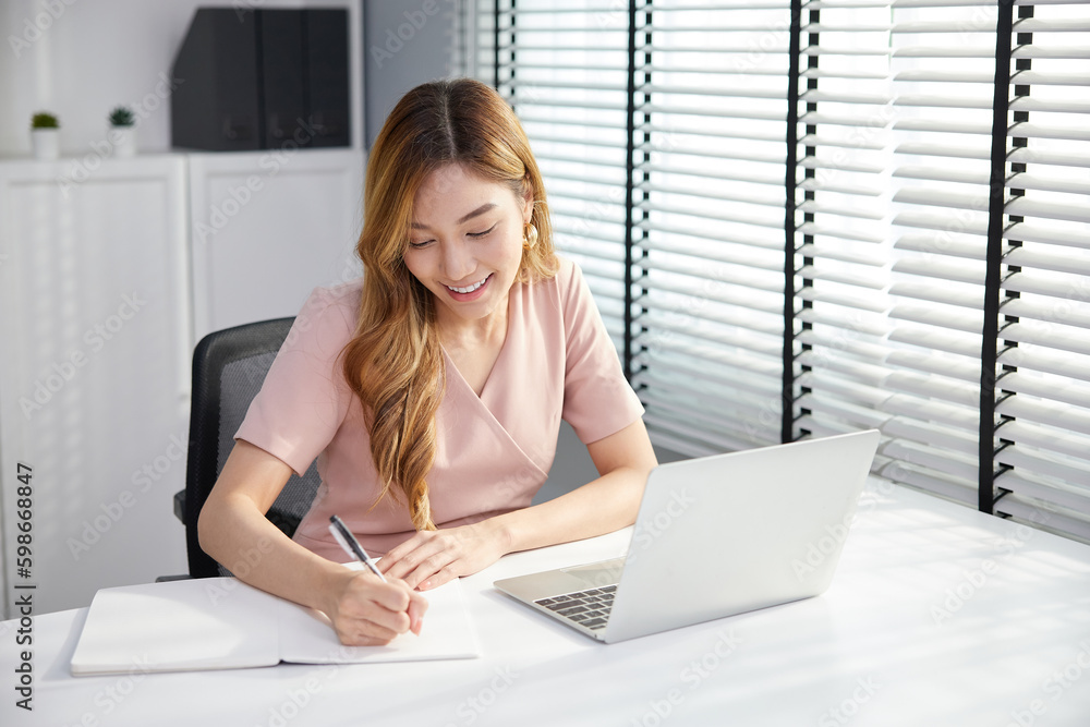 businesswoman using laptop computer and writing on notebook in the office businesswoman using laptop computer and writing on notebook in the office