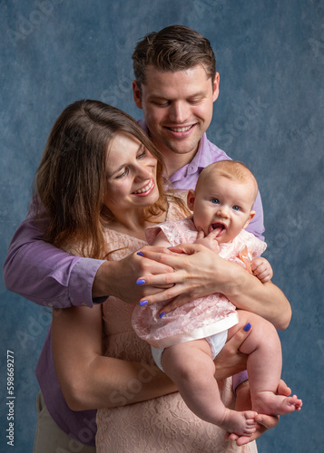 Mom and dad hold their little daughter in their arms and look at her tenderly. Love of young parents. Studio shooting