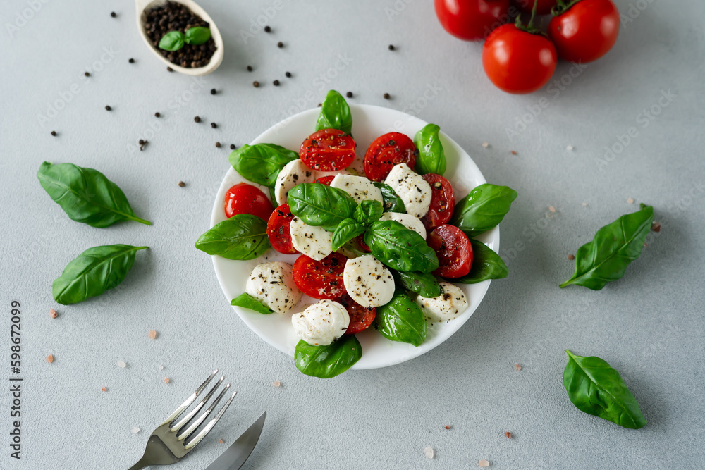 Caprese salad with ripe tomatoes and mozzarella cheese with fresh basil leaves on light background. Italian food Caprese salad with ripe tomatoes and mozzarella cheese with fresh basil leaves on light background. Italian food