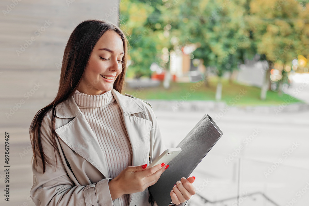 woman holding smartphone and a folder of an office building woman holding smartphone and a folder of an office building