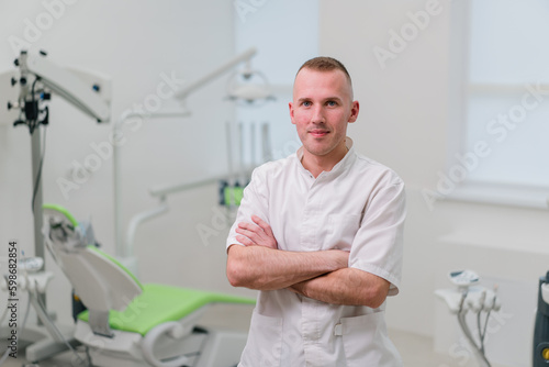 portrait of a handsome young smiling dentist doctor standing in the dental office before starting the procedure