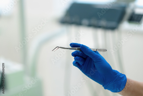 Professional dentist doctor holds working tools forceps in gloved hand before procedure in clinic close-up