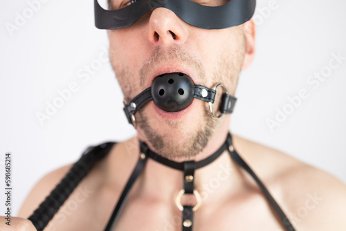 Muscular man in mask wearing leather harness and ball gag on white background. photo